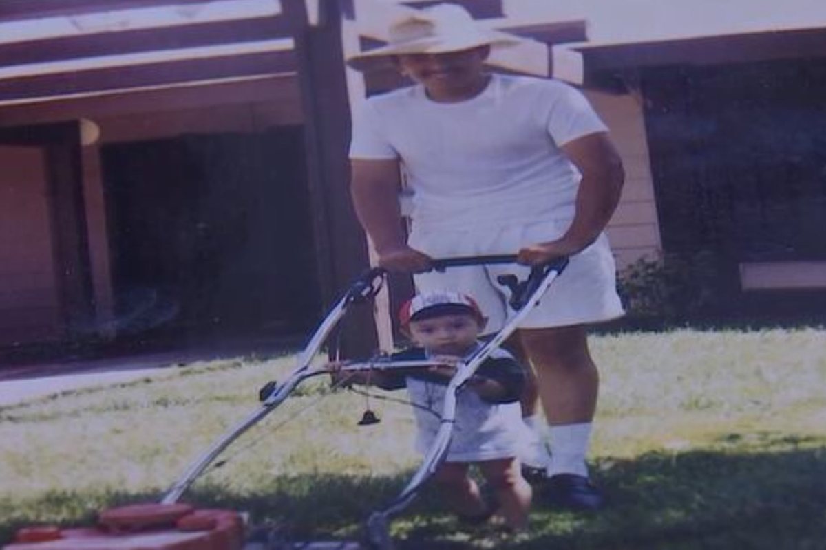 A young Edgar Andres Larios pushing a lawnmower with his small son at his feet